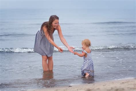 Happy Mother And Small Daughter Go Along The Seashore Stock Photo