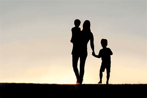 Silhouette Of Walking Mother And Young Children Holding Hands At Stock