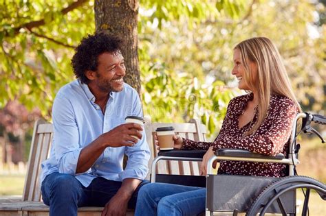 Mature Couple With Woman Sitting In Wheelchair Talking And Drinking