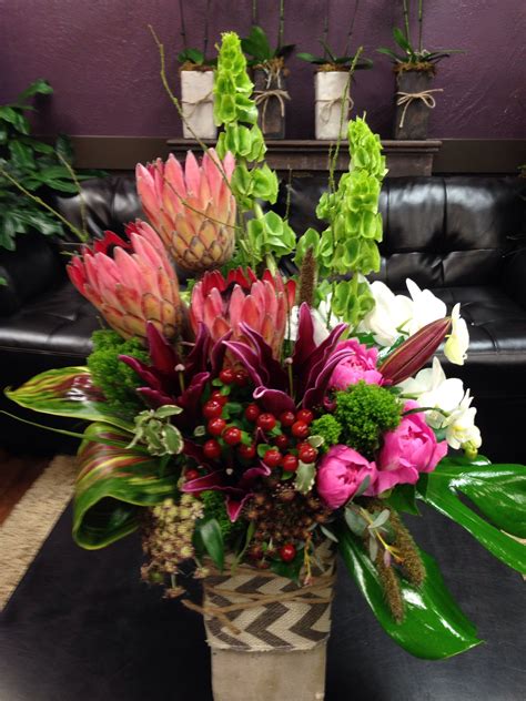 tropical floral arrangement with protea orchids peonies belles of ireland and ti leaves