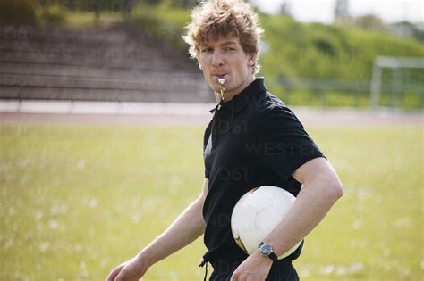 Referee Blowing Whistle While Carrying Soccer Ball On Field Stock Photo