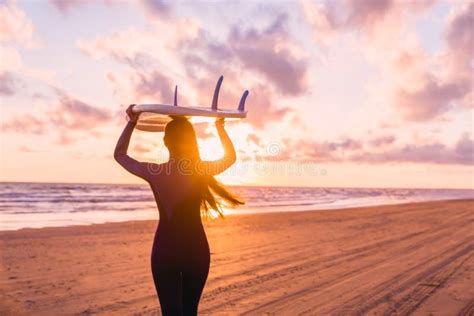 Beautiful Young Woman Surf Girl In Wetsuit With Surfboard On A Beach At