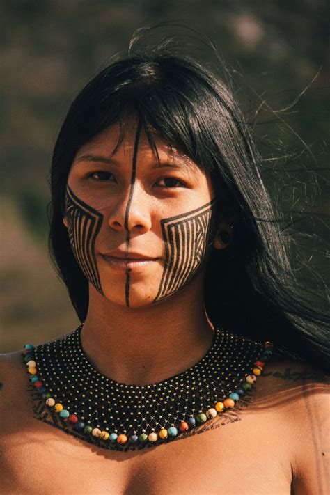 A Native American Woman With Painted On Her Face And Chest Is Looking At The Camera
