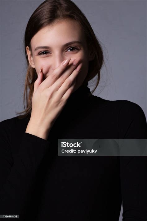 Test Shoot Of A Smiling Brunette Girl Covering Her Lips Posing Against
