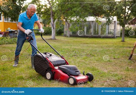 Positive Elderly Man With Lawnmower When Mowing The Lawn Stock Photo
