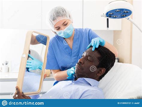 Cosmetologist Examining Male Client Face Before Procedure In Clinic