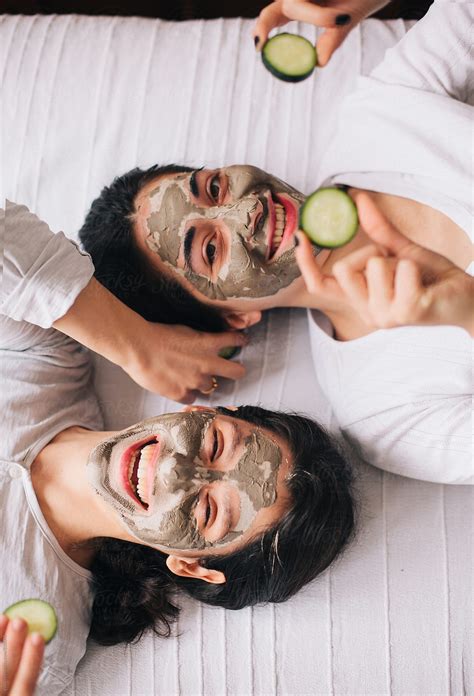 Two Beautiful Happy Female Friends With Facial Masks Lying On The Bed By Stocksy Contributor
