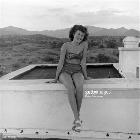 A Woman In A Bathing Suit Sitting On The Edge Of A Pool With Mountains In The Background