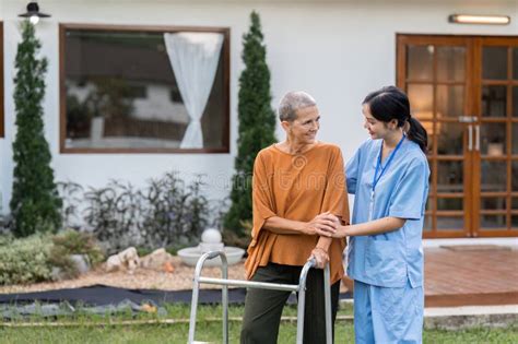 Nurse Or Caregiver Help Elderly Walk By Using Walker In Garden Stock