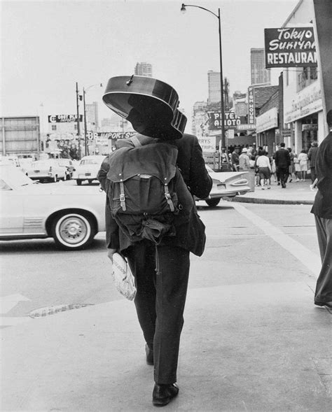 Black And White Photograph Of Man Walking Down The Street Wearing A