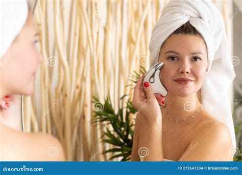 An Attractive Woman Does A Facial Massage With A Microcurrent Massager In Front Of A Bathroom