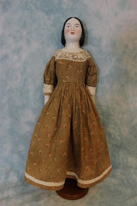 The Doll Is Wearing A Brown Dress With White Trim