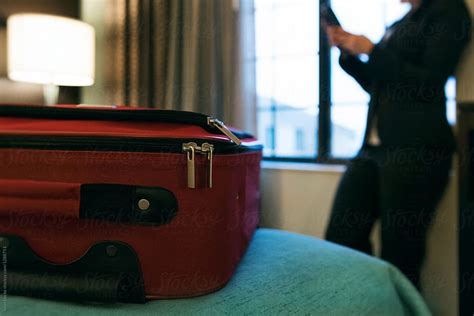 Business Luggage On Bed While Woman Checks Phone By Window Del