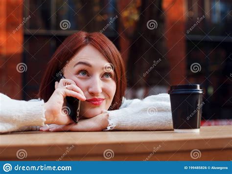 woman leans on bar table at outdoor cafe terrace and speacks on a phone with funny emotional