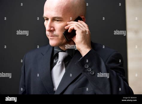 Bald Man In His Late 40s Wearing A Dark Suit Speaking On A Cell Phone