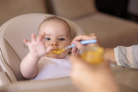 Happy Baby Eating Porridge And Sitting In High Chair Stock Photo