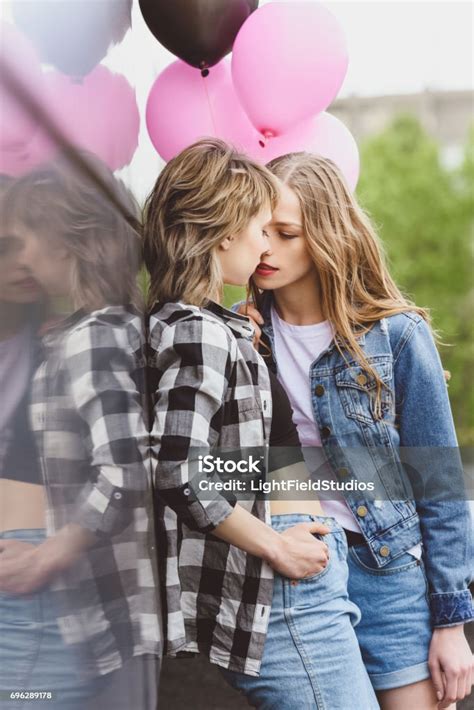 Young Casual Lesbian Couple Kissing And Holding Air Balloons Outdoors