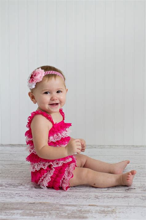 A Baby Girl Sitting On The Floor Wearing A Pink Dress And Smiling At