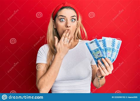 Young Caucasian Woman Holding 1000 Hungarian Forint Banknotes Covering Mouth With Hand Shocked