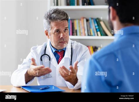 Mature Doctor Explaining Treatment To Patient At Office Of Hospital