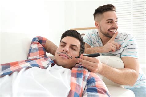 man drawing mustache on face of sleeping friend indoors april fool`s