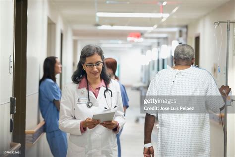 Female Doctor Assisting Senior Patient Walking With Iv Drip In Hospital