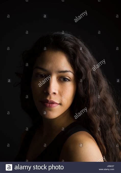 portrait pensive latina woman with long curly hair looking over shoulder against black