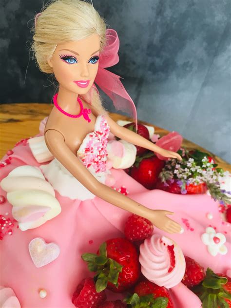 A Barbie Doll Sitting On Top Of A Pink Cake Covered In Strawberries And Icing