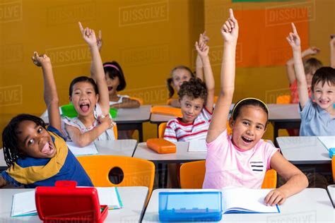 Happy Children Raising Their Hands In Classroom Stock