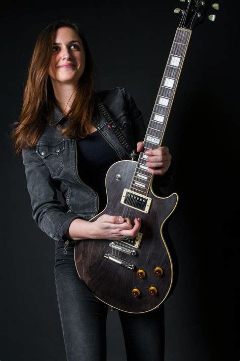 A Woman Is Holding An Electric Guitar In Her Right Hand And Posing For