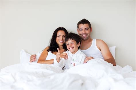 Criança com o polegar acima e seus pais na cama Foto Premium
