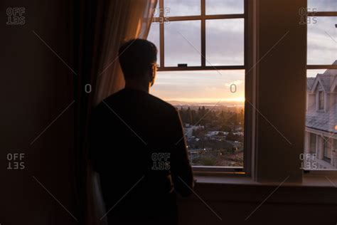 Man Looking Out A Window At The Sunset In Berkeley California Stock
