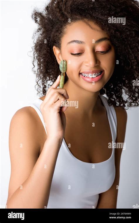 beautiful smiling african american girl with braces using natural massager isolated on grey