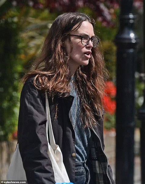 A Woman With Long Hair And Glasses Is Walking Down The Street Carrying A White Bag