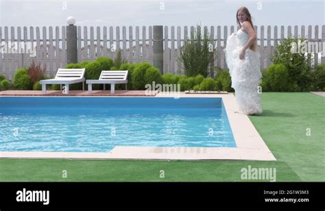 Young Blonde Girl In A White Wedding Dress Posing Beside Swimming Pool