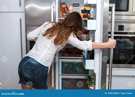 Modern Long Haired Woman Standing In The Kitchen And Open Refrigerators