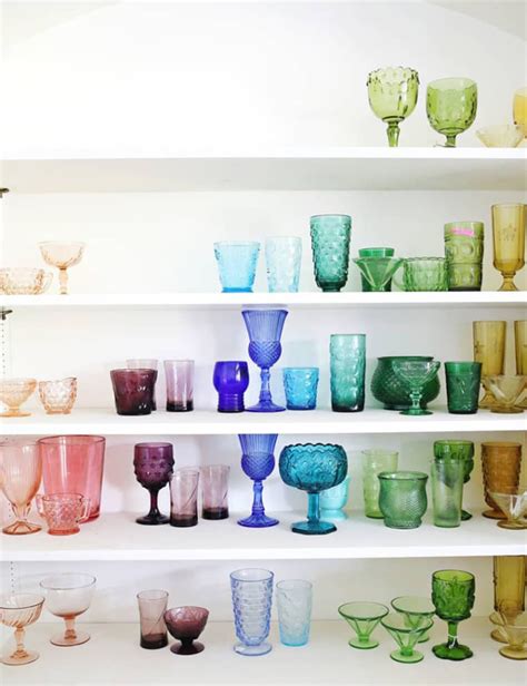Many Different Colored Glasses Lined Up On The Shelves In A Room With White Shelving