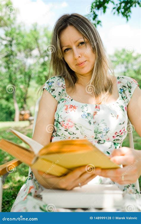 Una Mujer En Libro De Lectura Del Vestido De La Flor Y El Sentarse Al Aire Libre Foto De Archivo