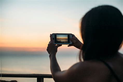 Woman Taking Pictures With Phone At Sea Sunset By Stocksy Contributor Marko Stocksy
