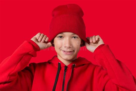 Smiling Teen Boy In A Red Knitted Hat And Red Hoodie Adjusting His Hat