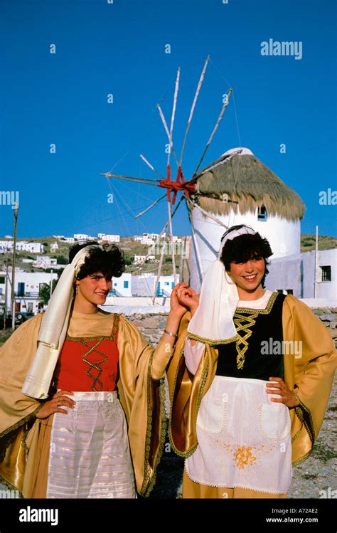 Windmills And Girls Wearing Traditional Greek Costumes On Mykonos
