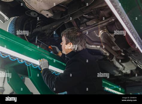 Side View Of Male Mechanic Examining Car With Hammer In Auto Repair