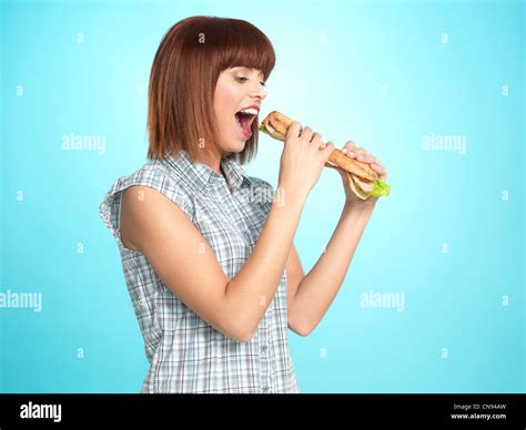Portrait Of Beautiful Young Woman Eating A Big Sandwich Smiling On Blue Background Stock