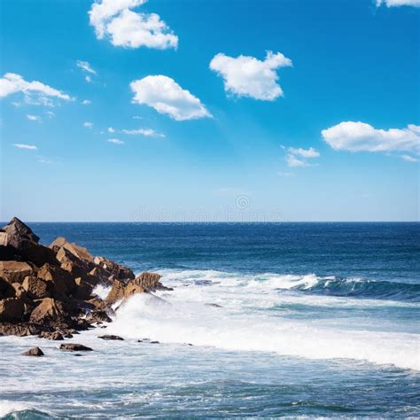 Beautiful Rocky Beach And Ocean Wave Under Blue Cloudy Summer Sky