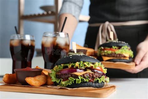 Woman With Black Burger Fries And Drinks Served On Table Stock Image