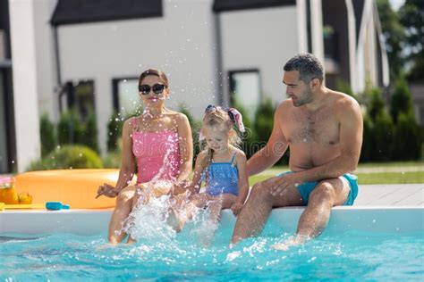 Father Splashing Water On His Daughter And Wife In The Swimming Pool