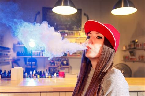 Young Pretty Woman In Red Cap Smoke An Electronic Cigarette At The Vape Shop Stock Image Image