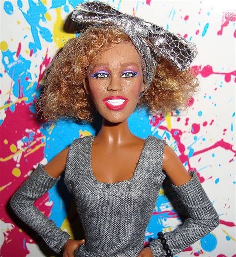 A Close Up Of A Barbie Doll With Paint Splattered On The Wall Behind Her