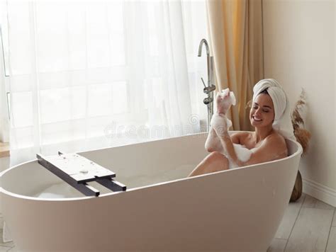 Joyful Young Caucasian Pretty Woman Lying In Bathtub With Foam Naked With Towel On Head Relaxing
