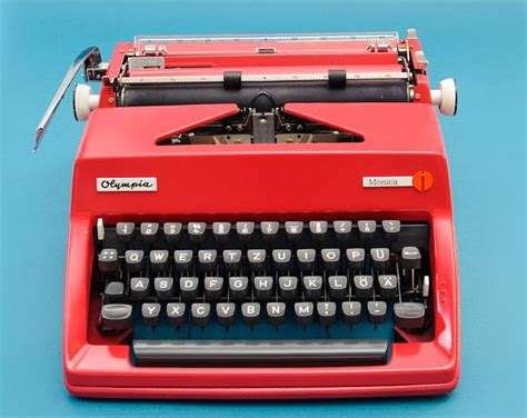 An Old Fashioned Red Typewriter Sitting On A Blue Surface With The Keys